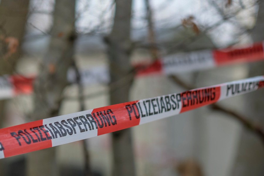 Ein Flatterband der Polizei ist als Absperrung um mehrere Bäume in einem Waldstück gewickelt, an dem auch ein Bauwagen und eine Holzhütte stehen.