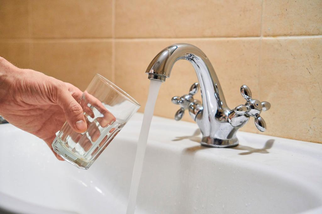 Glas wird unter fließenden Wasserhahn gehalten