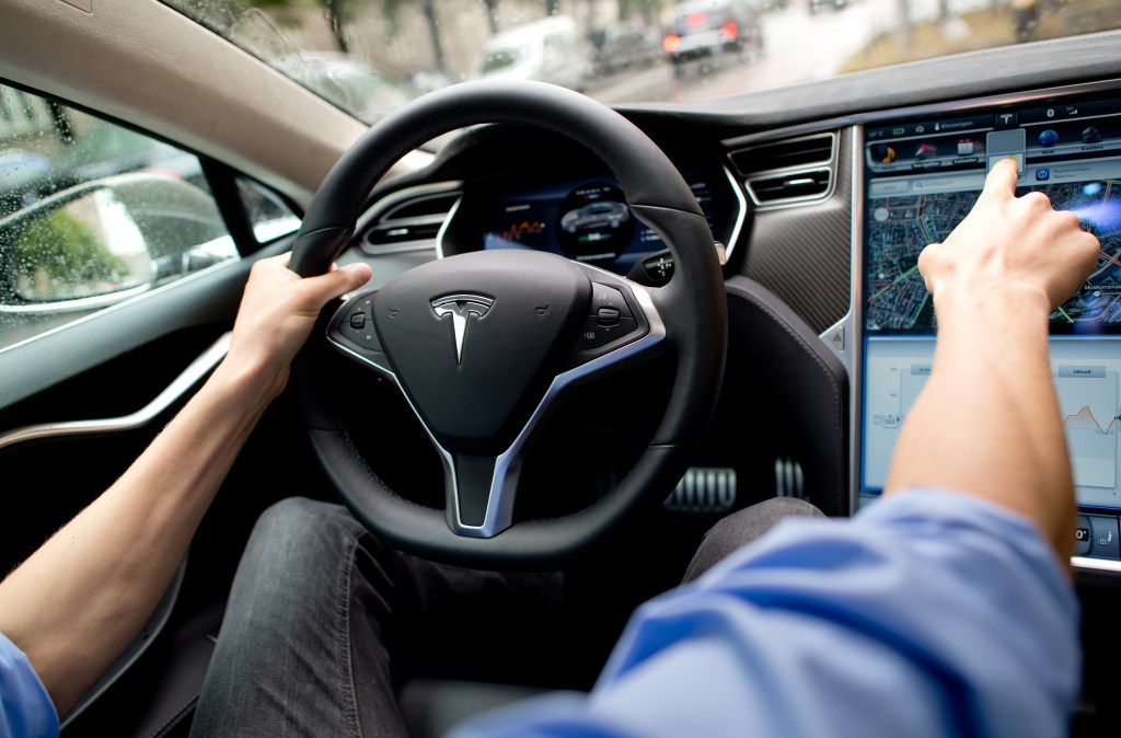 Mann sitzt hinterm Tesla Steuer und zeigt auf Cockpit