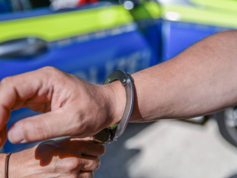 Mann werden Handschellen vor Polizeiauto angelegt