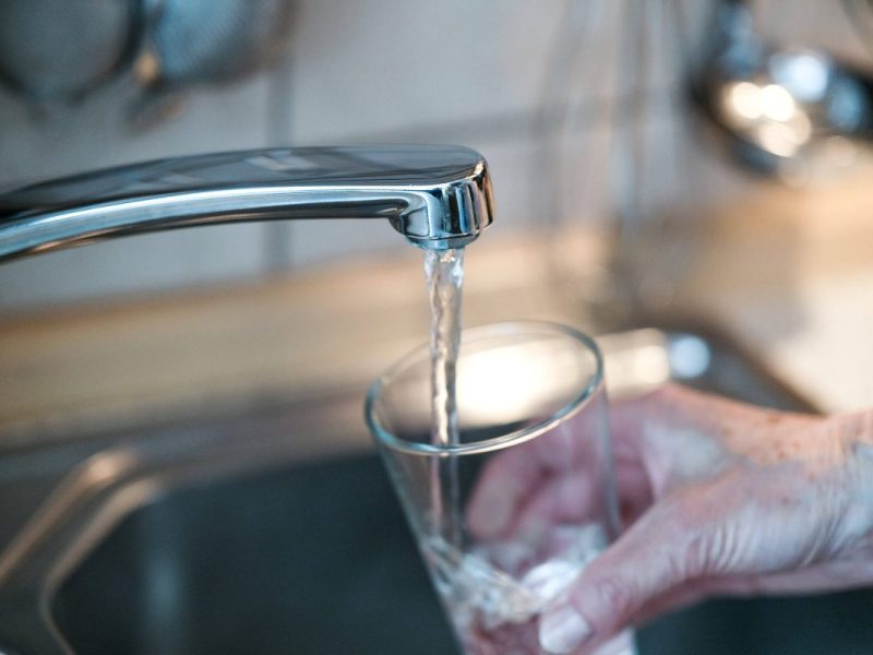 Frau hält Glas unter den Wasserhahn