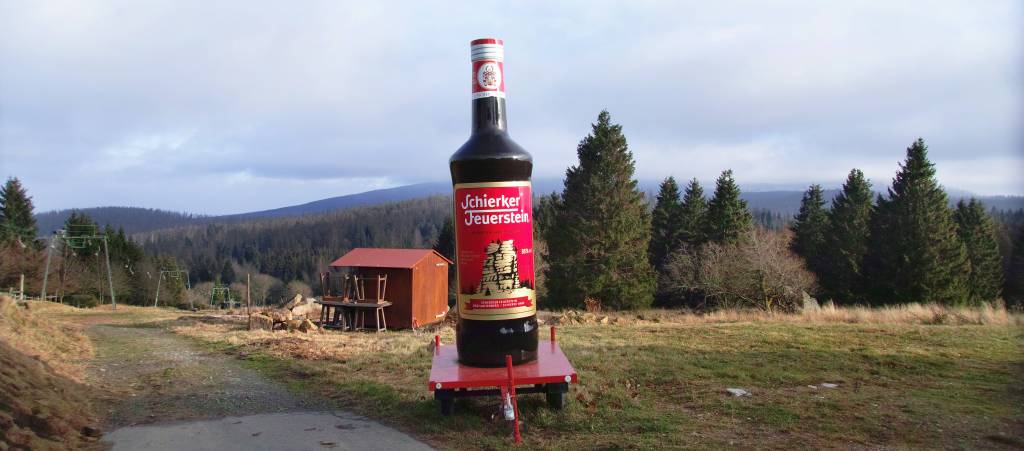 Fotoeinblicke im Goslars-Ort Torfhaus. Flasche Schierker Feuerstein auf Skipiste vor Wolkenverhangenem Brocken.