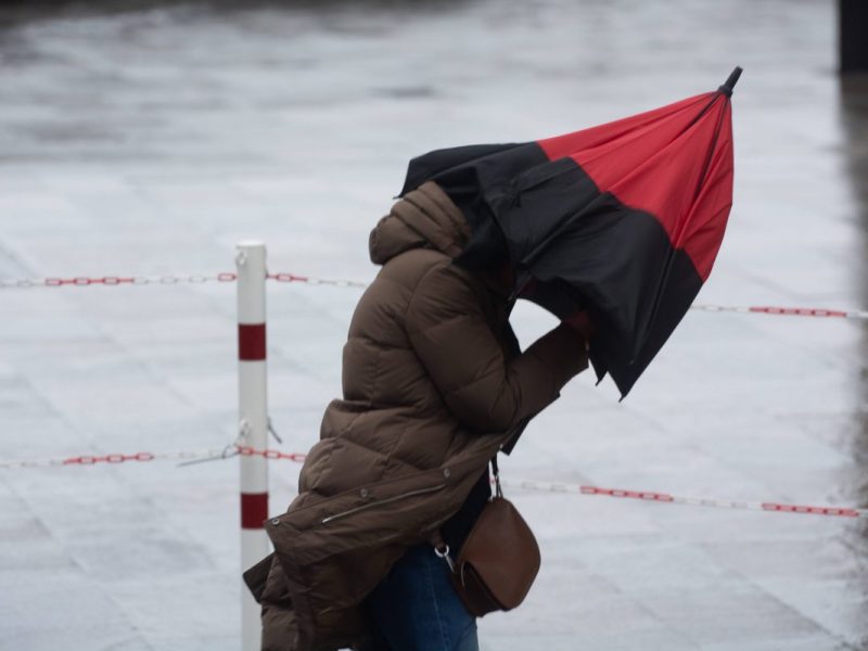 Eine Frau hat aufgrund starker Windböen Probleme ihren Regenschirm festzuhalten. (Symbolbild) für das Wetter in Niedersachsen.