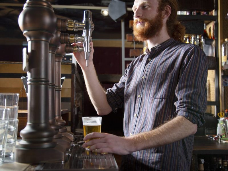 Ein bärtiger Mann zapft ein Bier am Zapfhahn, (Symbolbild)