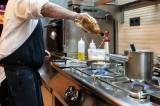 A chef in a professional kitchen is focused on pouring alcohol into a pan,