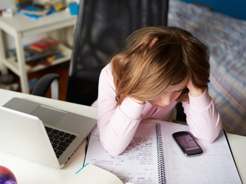 Mädchen sitzt am Schreibtisch mit einem Laptop und Handy